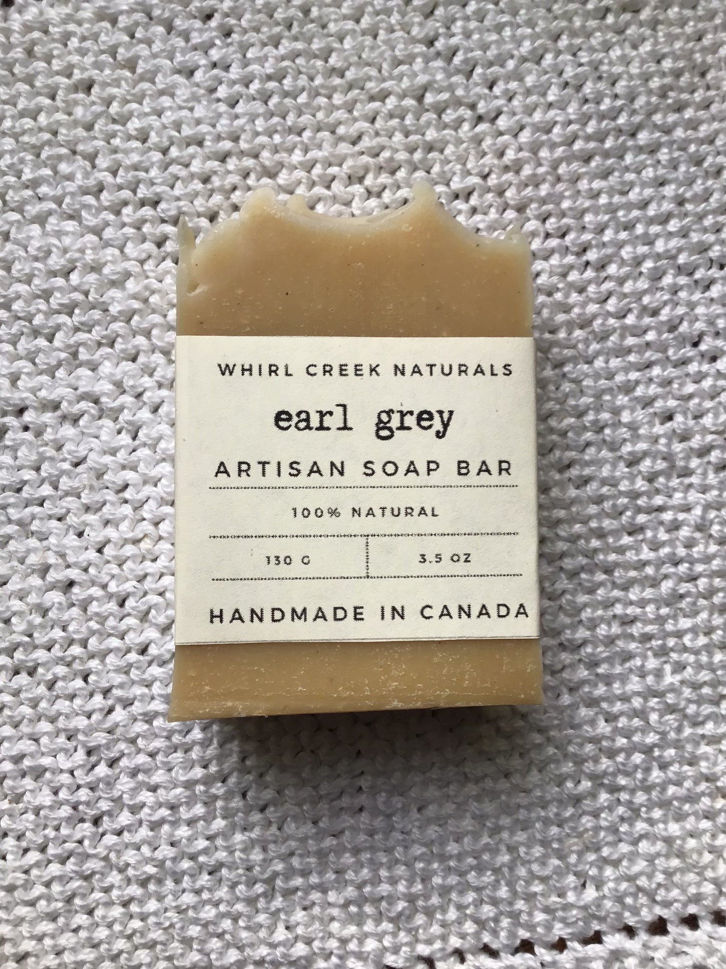 bar of soap placed on knit white cotton cloth. Label wrapped around the middle bar has earl grey artisan soap bar, 130 grams and handmade in Canada printed on in. 