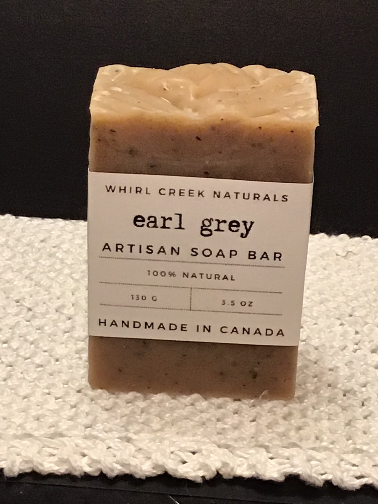 bar of soap placed on knit white cotton cloth. Label wrapped around the middle bar has earl grey artisan soap bar, 130 grams and handmade in Canada printed on in.